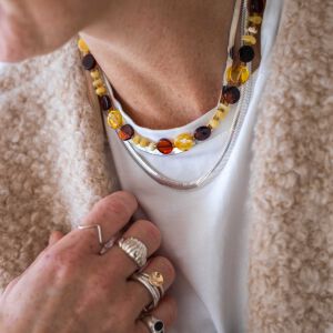 Zbliżenie na detal płaskich bursztynów ułożonych na szyi modelki w formie naszyjnika z kolorowych bursztynów.
