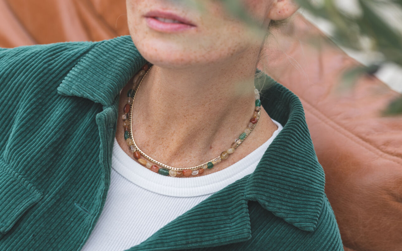 Naszyjnik z kolorowych kwarców prezentowany na szyi modelki w połączeniu z delikatnym naszyjnikiem typu snake, tworzący nowoczesną warstwową stylizację.