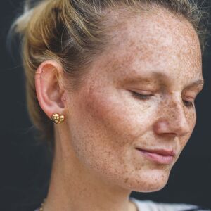 Kolczyki asymetryczne z nieregularnym połyskiem pokazane na tle skóry w naturalnym świetle
